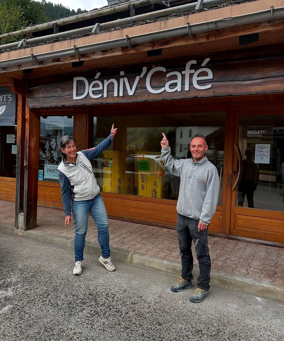 Anne et Fabien, les bras levés devant la façade du Déniv’Café